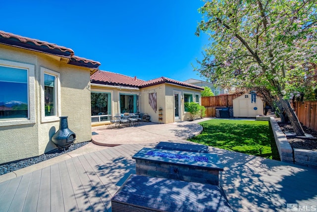back of property featuring a fenced backyard, a storage shed, stucco siding, a wooden deck, and an outdoor fire pit