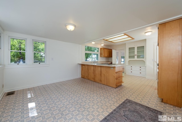 kitchen with a peninsula, light countertops, baseboards, and brown cabinetry