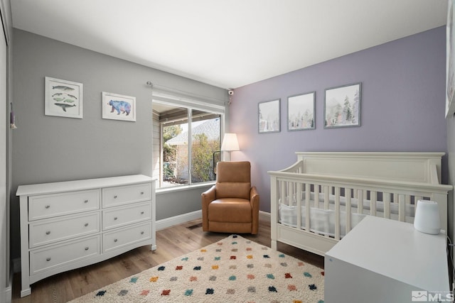 bedroom with a nursery area, baseboards, wood finished floors, and visible vents