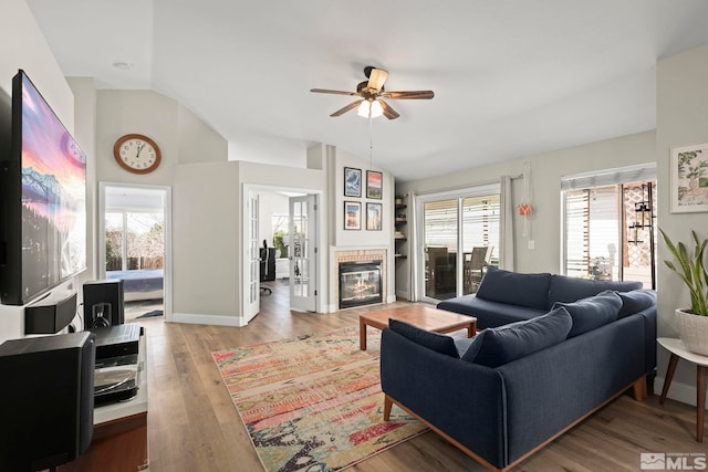 living area featuring lofted ceiling, a tile fireplace, light wood finished floors, a ceiling fan, and baseboards