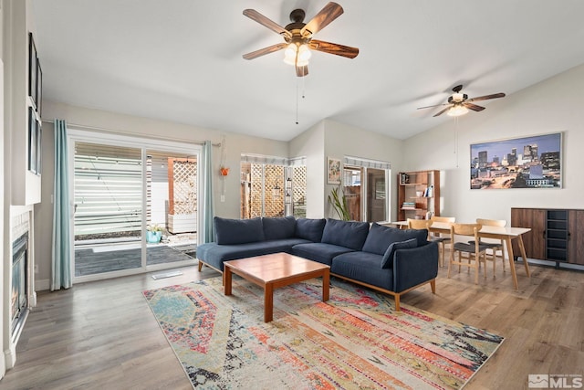 living area with ceiling fan, lofted ceiling, a glass covered fireplace, and wood finished floors