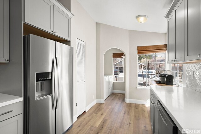kitchen featuring separate washer and dryer, light wood-type flooring, arched walkways, stainless steel appliances, and baseboards