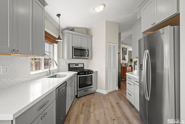 kitchen with light wood-style floors, appliances with stainless steel finishes, decorative backsplash, and a sink