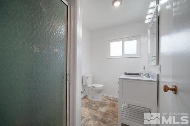 full bathroom featuring stone finish floor, toilet, vanity, baseboards, and a stall shower