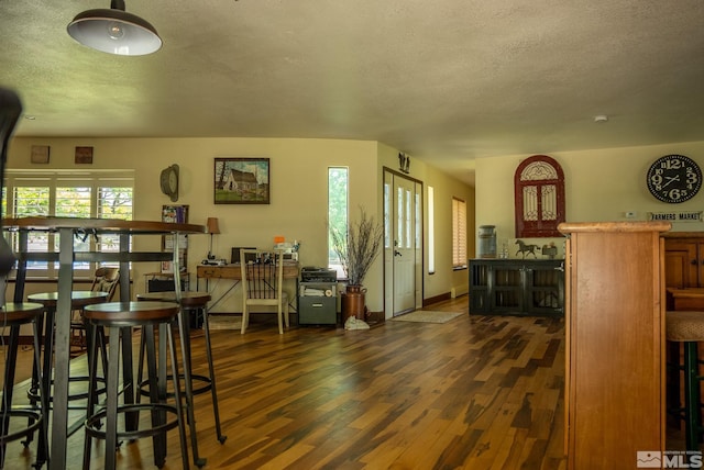 living room featuring dark wood finished floors, baseboards, a bar, and a textured ceiling
