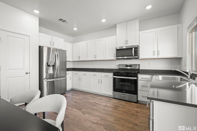 kitchen with white cabinets, dark countertops, stainless steel appliances, and a sink