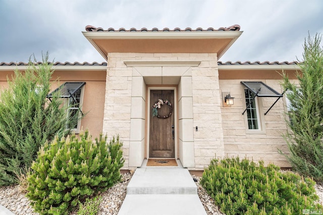 view of exterior entry with stucco siding, a tiled roof, and stone siding