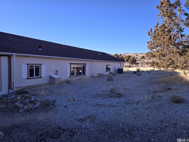 rear view of house featuring central AC, a mountain view, and roof with shingles