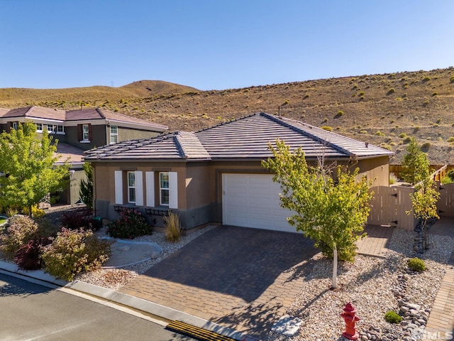 view of front facade with a tile roof, decorative driveway, an attached garage, a mountain view, and stucco siding