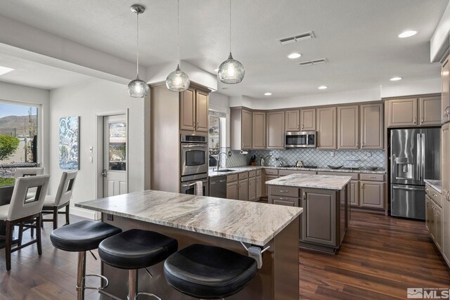 kitchen featuring decorative backsplash, stainless steel appliances, a kitchen island, and dark wood-style floors