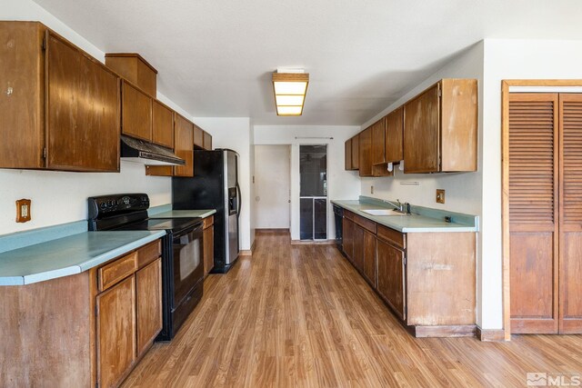 kitchen with black appliances, a sink, under cabinet range hood, and light wood-type flooring
