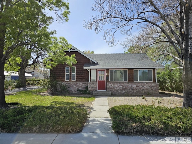 view of front of home with a front yard, roof with shingles, and brick siding