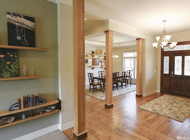 foyer featuring crown molding, ornate columns, an inviting chandelier, and hardwood / wood-style flooring
