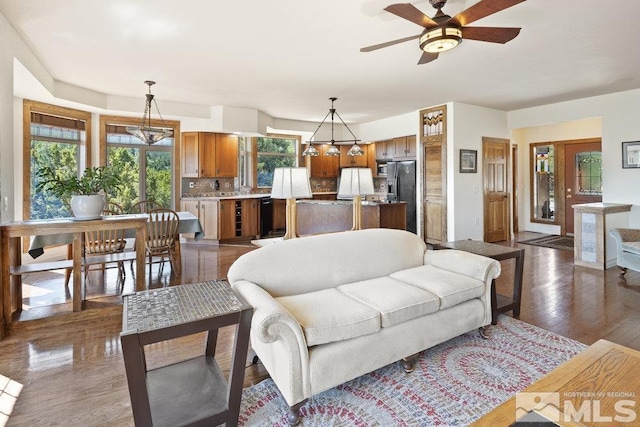living room featuring dark wood-style floors, a ceiling fan, and a healthy amount of sunlight