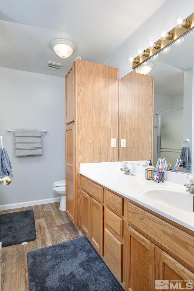 full bathroom featuring a shower with shower door, visible vents, wood finished floors, and a sink