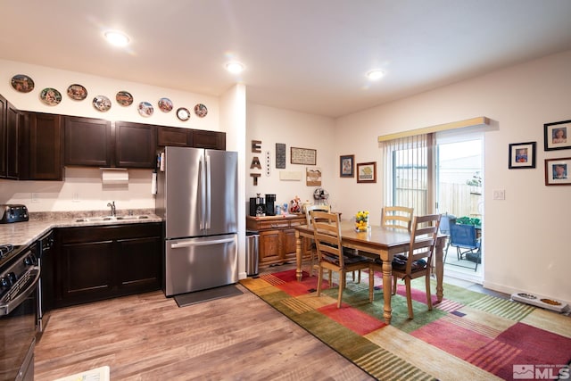 kitchen featuring black range, freestanding refrigerator, dark brown cabinets, a sink, and light wood-type flooring