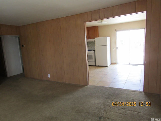 empty room featuring wooden walls, light tile patterned flooring, and light colored carpet