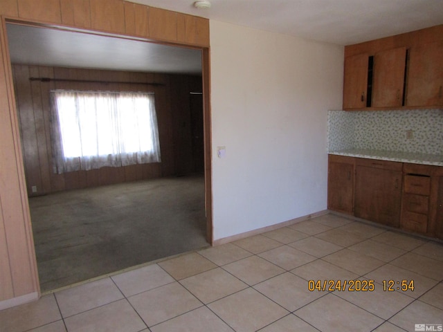 kitchen featuring decorative backsplash, light countertops, light tile patterned flooring, light carpet, and brown cabinetry