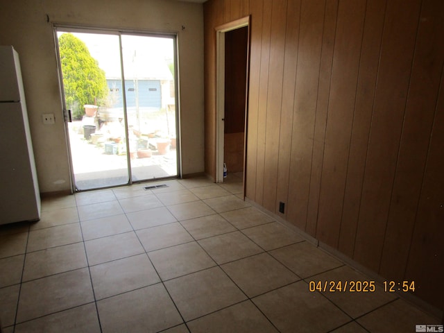 empty room featuring visible vents, light tile patterned floors, and wood walls