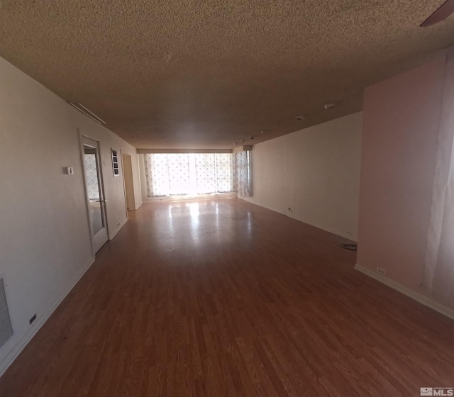 empty room with a textured ceiling, baseboards, and dark wood finished floors