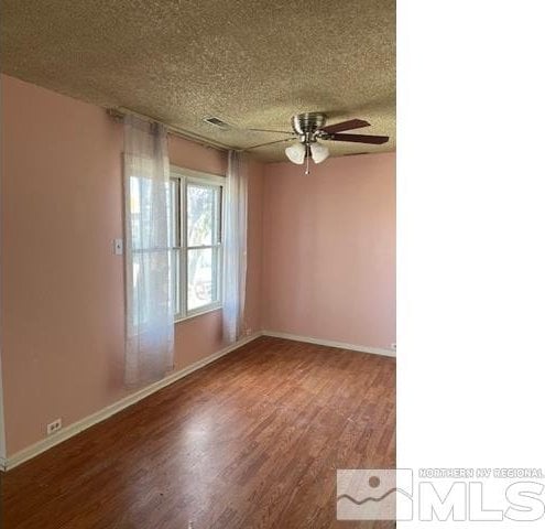 empty room featuring a ceiling fan, a textured ceiling, wood finished floors, and baseboards