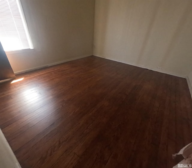 spare room featuring dark wood-type flooring and baseboards