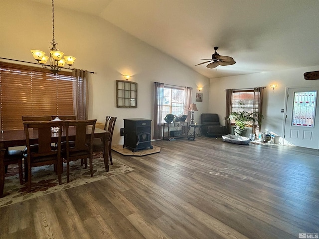 dining room with dark wood finished floors, a wood stove, ceiling fan with notable chandelier, and vaulted ceiling