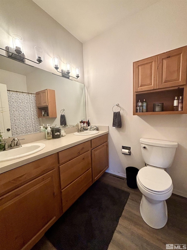 bathroom featuring wood finished floors, toilet, double vanity, and a sink