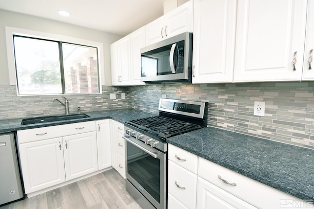 kitchen featuring white cabinets, a sink, light wood finished floors, dark stone counters, and stainless steel appliances