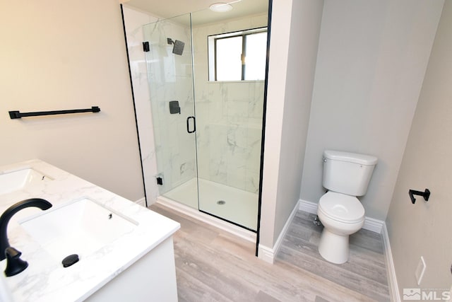 bathroom featuring double vanity, wood finished floors, a sink, toilet, and a marble finish shower