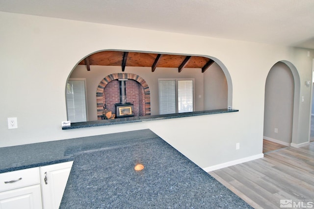 interior space with a wood stove, beamed ceiling, wood ceiling, white cabinets, and light wood finished floors