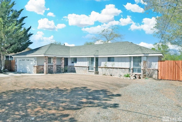 ranch-style home with board and batten siding, driveway, brick siding, fence, and an attached garage