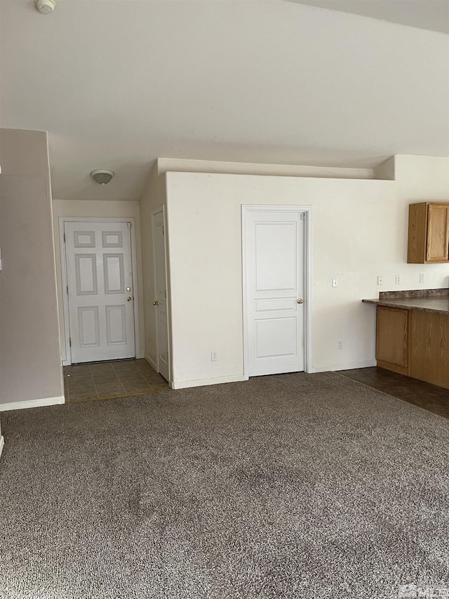 unfurnished living room with baseboards and dark carpet