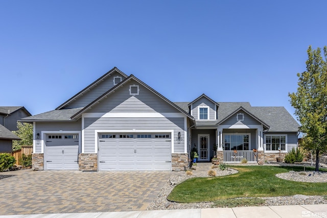 craftsman-style house with covered porch, a garage, decorative driveway, a front lawn, and stone siding