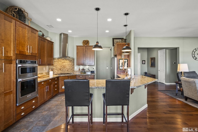 kitchen with visible vents, a breakfast bar area, wall chimney exhaust hood, brown cabinets, and appliances with stainless steel finishes