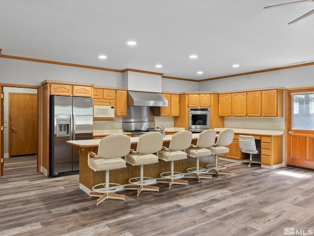 kitchen featuring crown molding, an island with sink, wall chimney range hood, light countertops, and stainless steel appliances