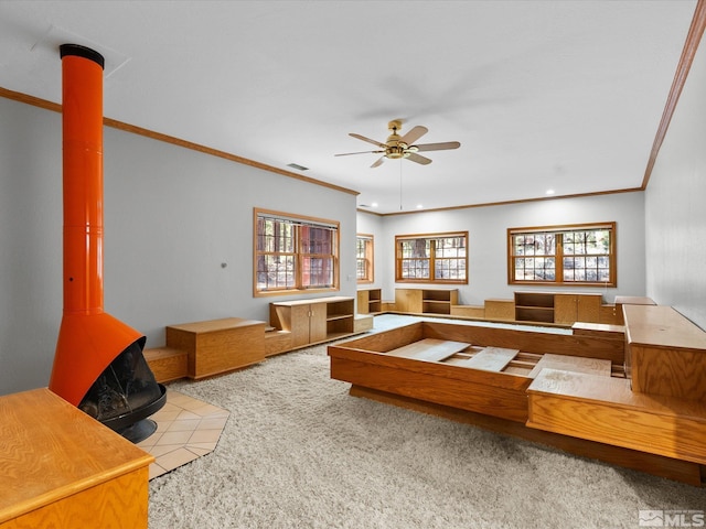 living area with ceiling fan, a wood stove, carpet, a healthy amount of sunlight, and ornamental molding