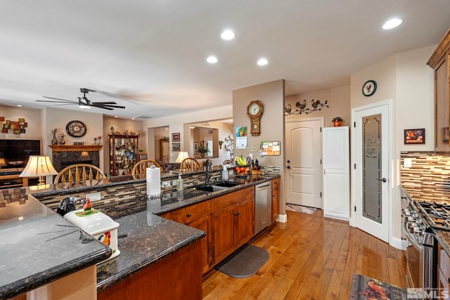 kitchen with ceiling fan, a fireplace, light wood-type flooring, a sink, and stainless steel appliances