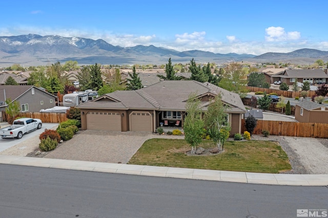 ranch-style house featuring fence, an attached garage, a front lawn, a mountain view, and decorative driveway