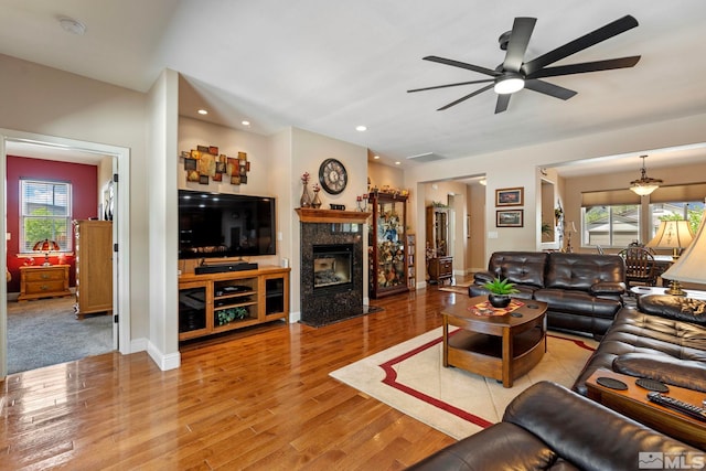 living area featuring a healthy amount of sunlight, light wood-style floors, a ceiling fan, and a premium fireplace