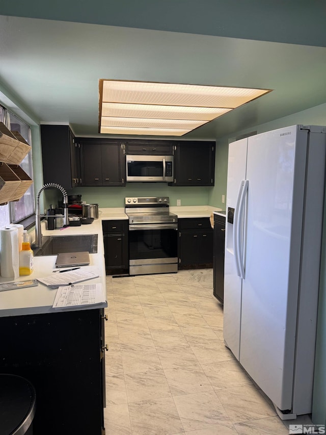 kitchen with light floors, light countertops, dark cabinetry, a sink, and stainless steel appliances