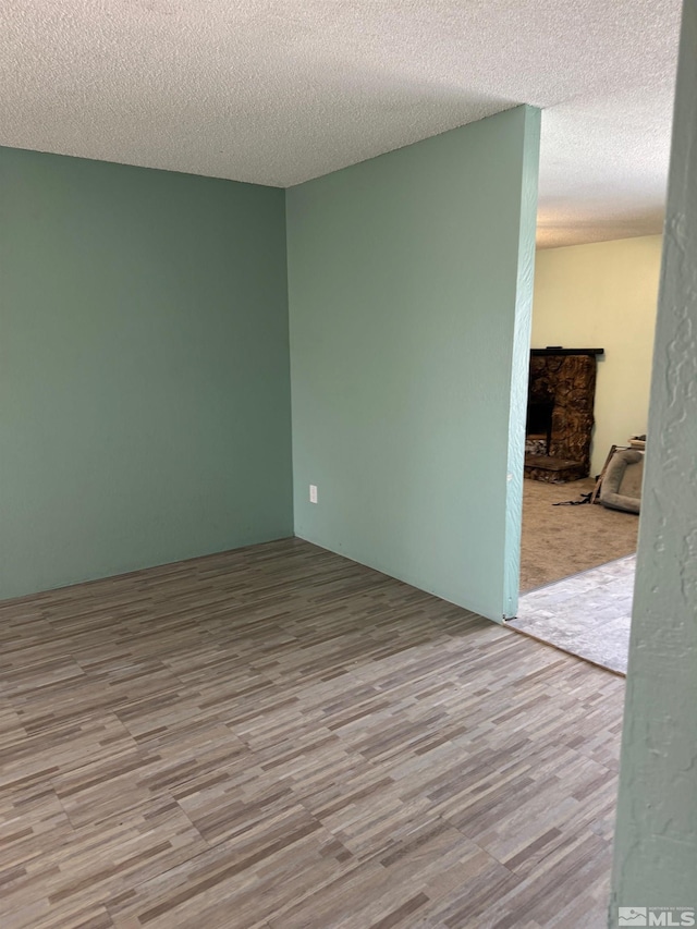 unfurnished room with a textured ceiling, a stone fireplace, and wood finished floors