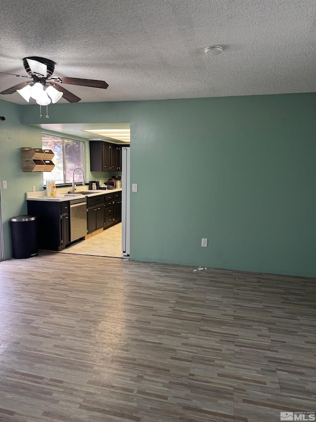 kitchen featuring a sink, light countertops, a textured ceiling, wood finished floors, and stainless steel dishwasher