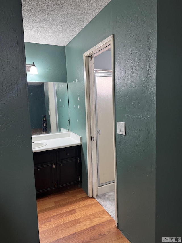 bathroom featuring a textured ceiling, a textured wall, wood finished floors, and vanity
