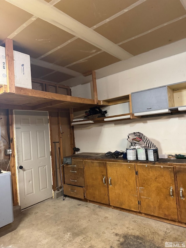 kitchen featuring brown cabinets, dark countertops, open shelves, and unfinished concrete flooring