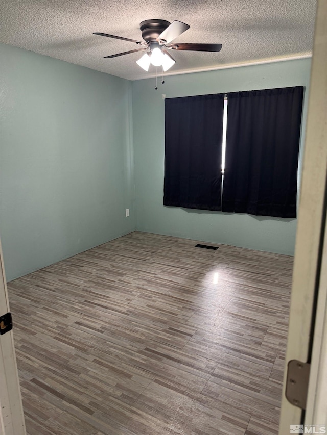 spare room featuring a textured ceiling, ceiling fan, visible vents, and wood finished floors