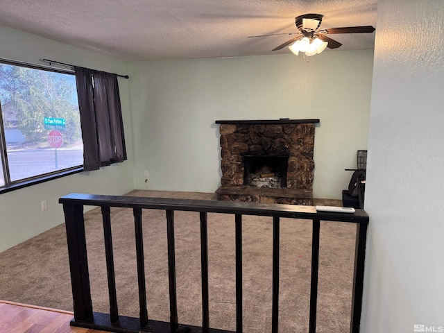 interior space with a stone fireplace, a textured ceiling, ceiling fan, and wood finished floors