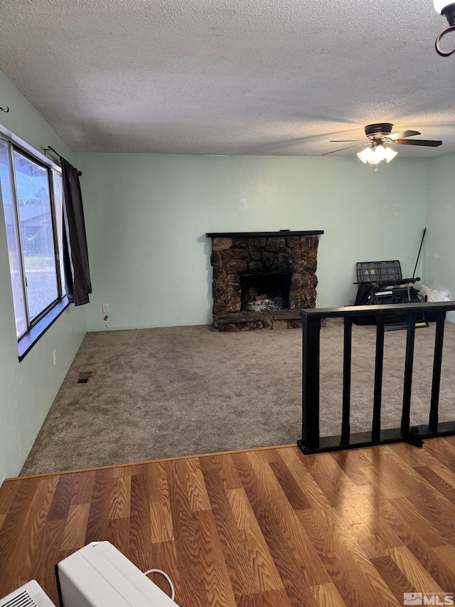 living area featuring ceiling fan, a textured ceiling, visible vents, a fireplace, and wood finished floors