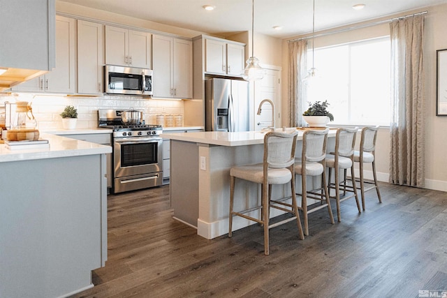 kitchen with a kitchen breakfast bar, appliances with stainless steel finishes, tasteful backsplash, light countertops, and dark wood-style floors