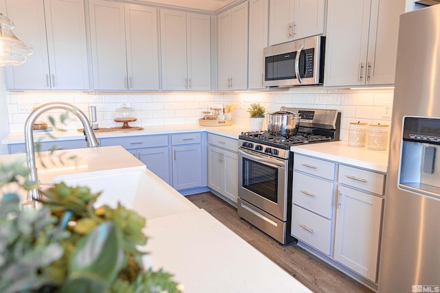 kitchen featuring backsplash, appliances with stainless steel finishes, hanging light fixtures, light countertops, and dark wood-style floors